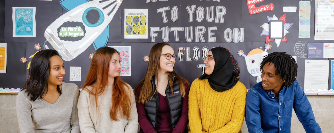 Five residents sitting in front of a bulletin board in residence.
