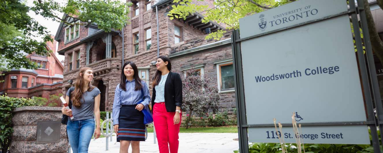 Three students walking in front of Woodsworth sign