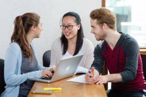 Three students in classroom smiling with laptop