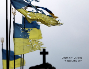 Torn Ukrainian flags near a graveyard.